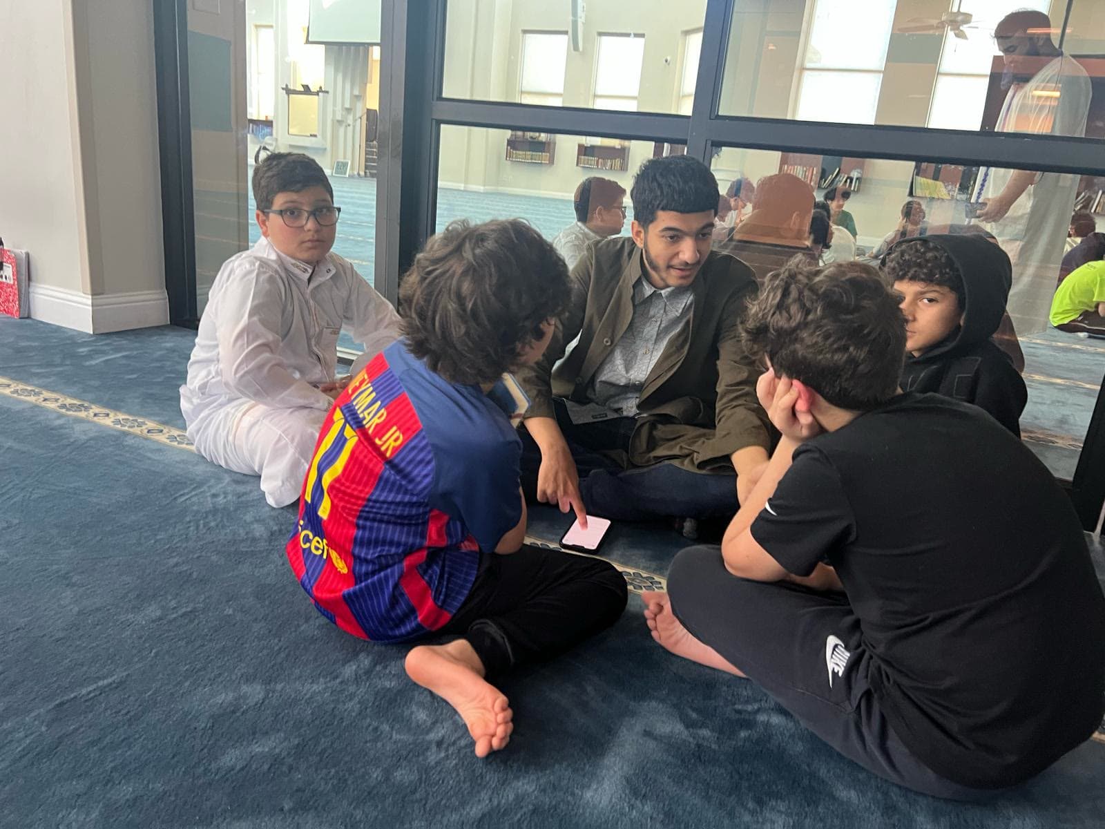 A teacher seated on the floor with a circle of young students, books open between them