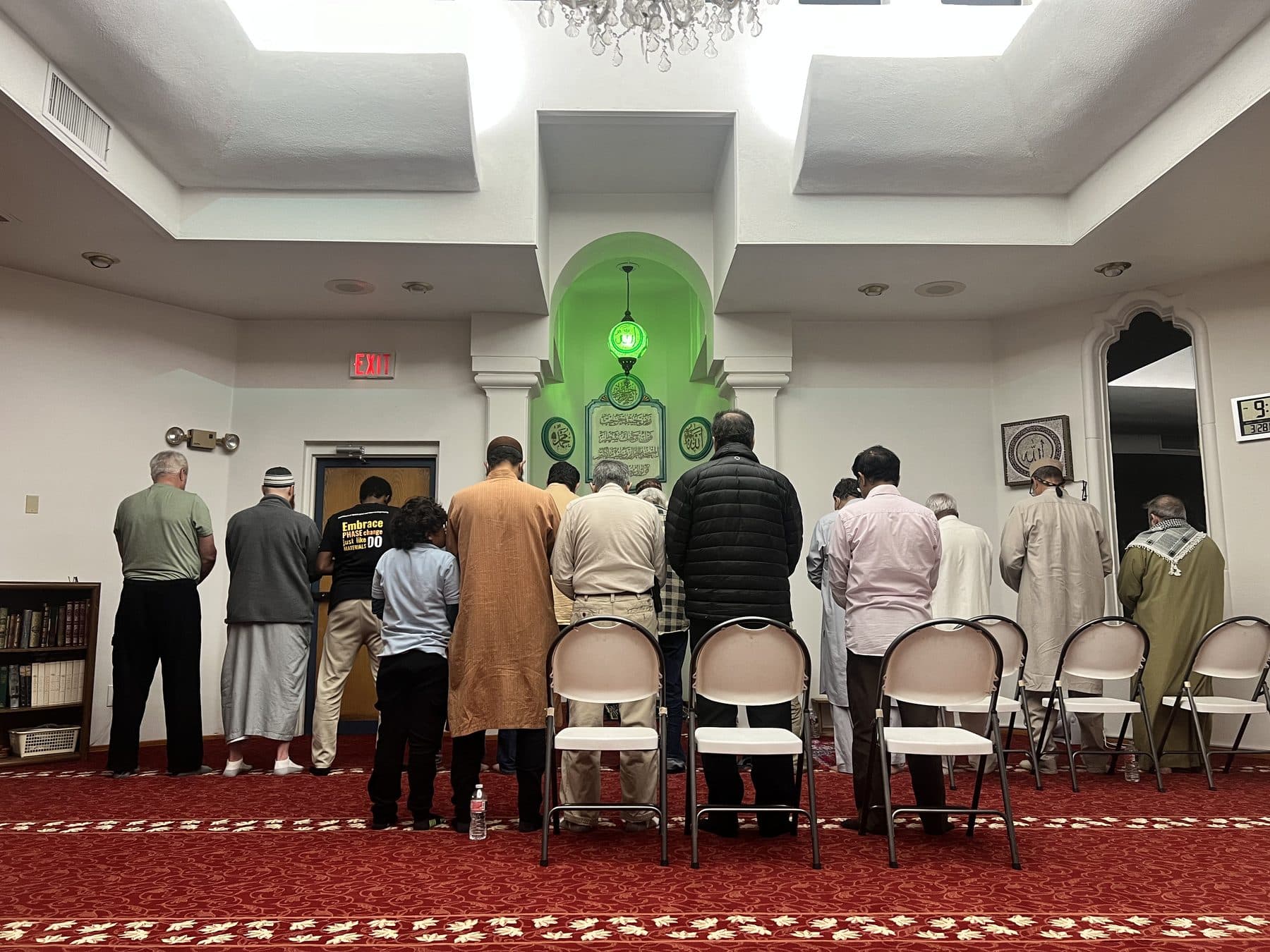 Worshippers praying in rows beneath an ornate green mihrab arch